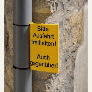 Gelbes 3D-gedrucktes Rohrschild „Bitte Ausfahrt freihalten! Auch gegenüber!“ an einem 100-mm-Regenrohr.